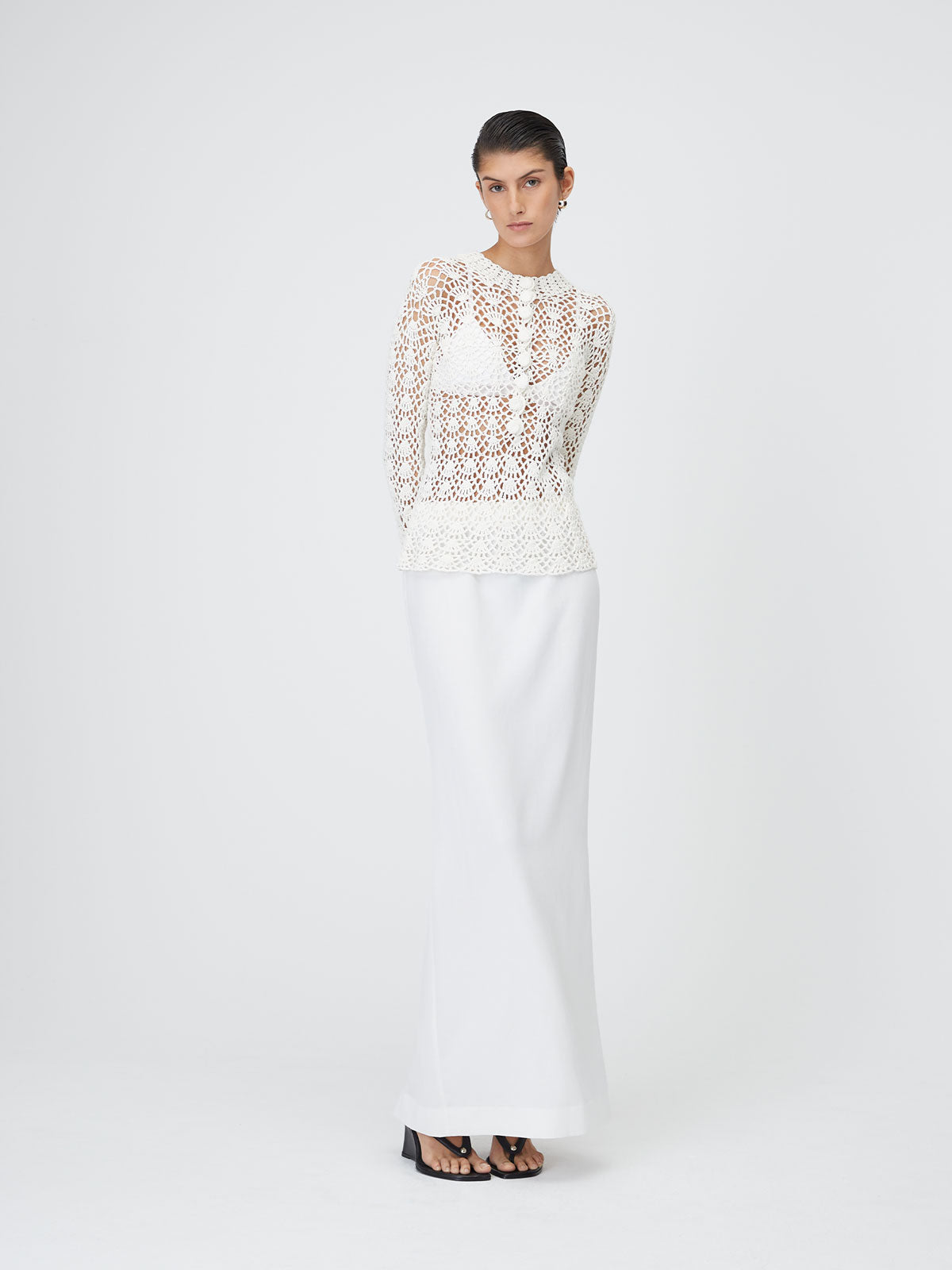 Front view of a model wearing the White 9 Crochet Top with her hands behind her back on top of a white background