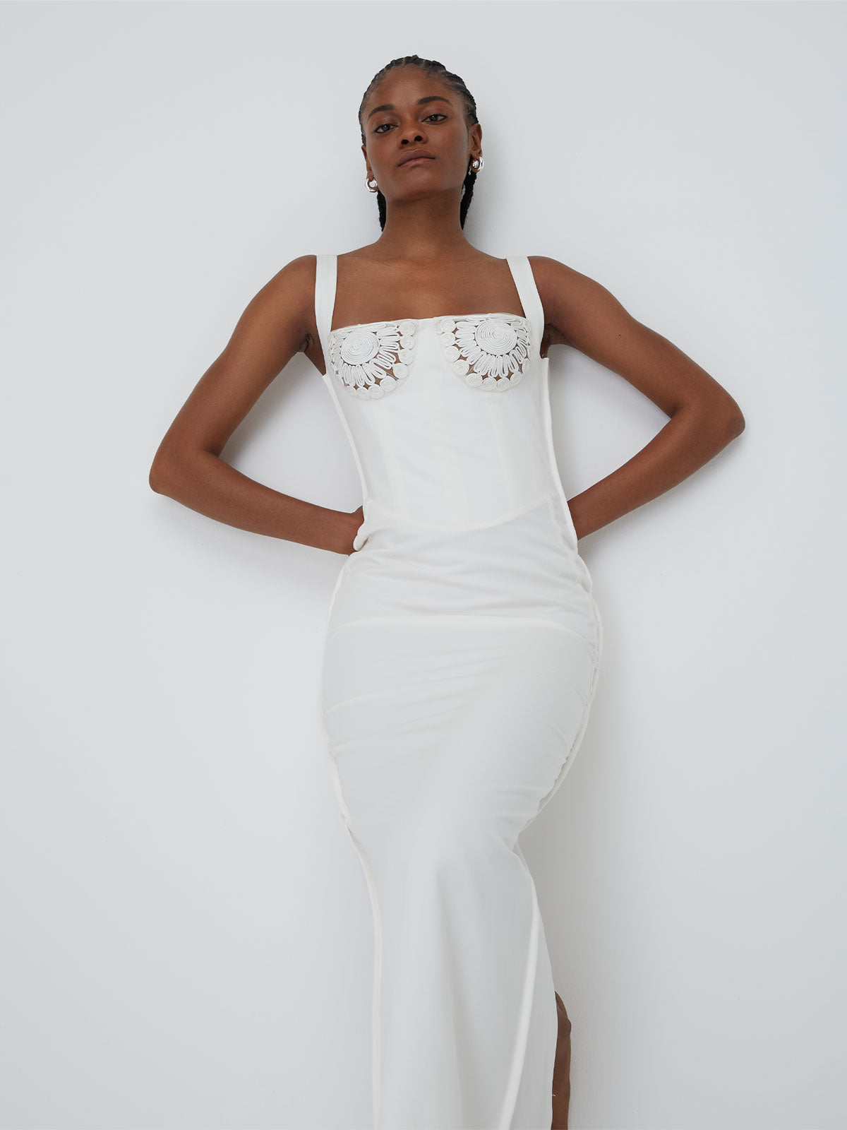 A female figure leaning back against a wall with her arms held behind her lower back wearing the White 09 Micah Dress