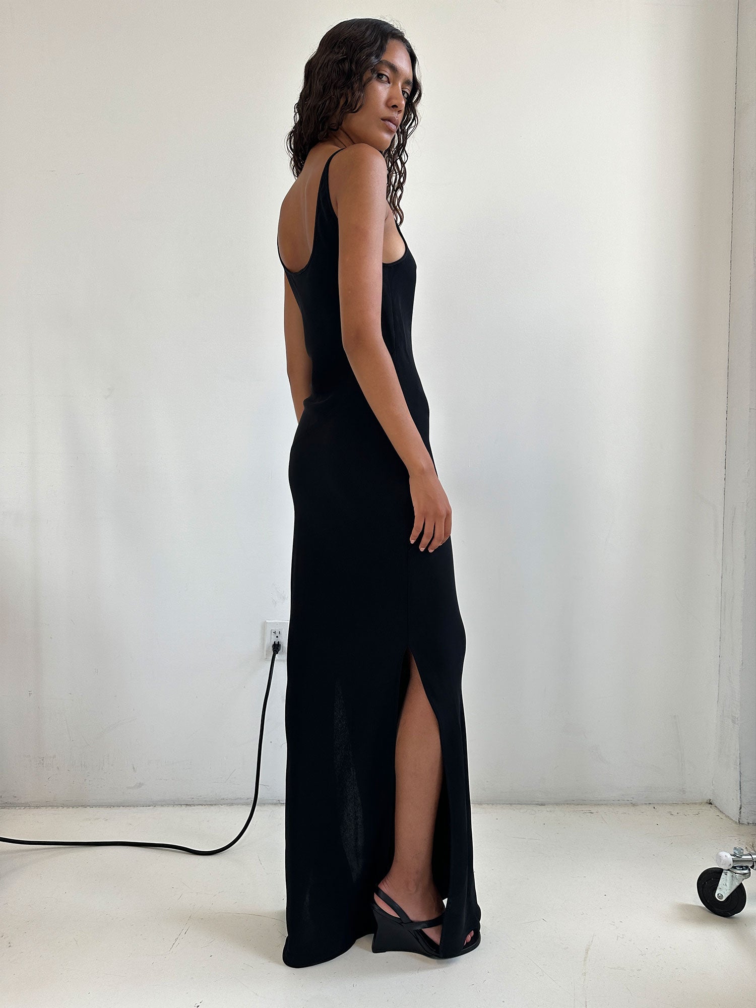 A woman looking over her shoulder wearing a Black Elemental Mala Slip and dark heels