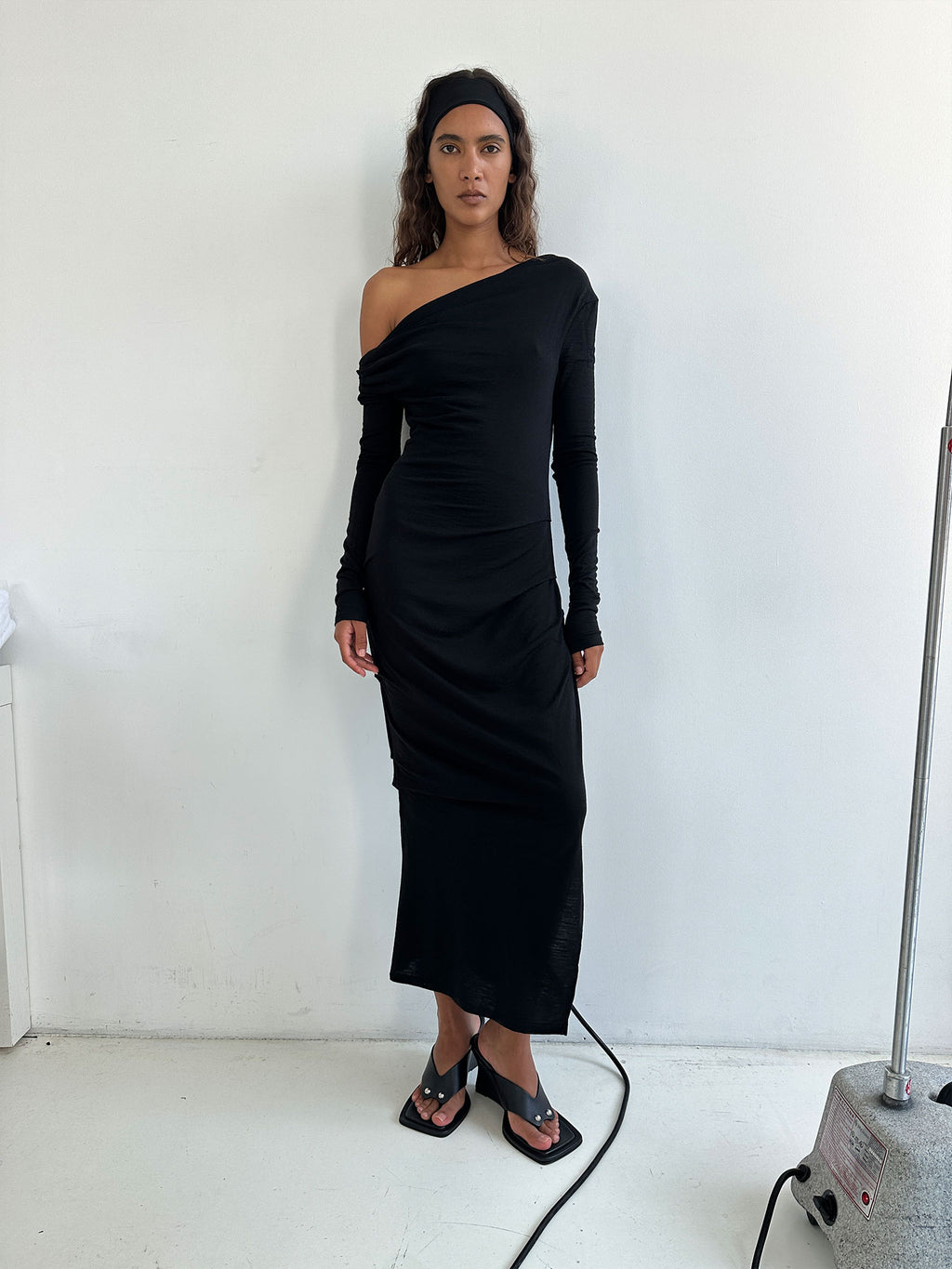 Model facing forwards standing against a grey wall wearing a Black Elemental Manahou Dress