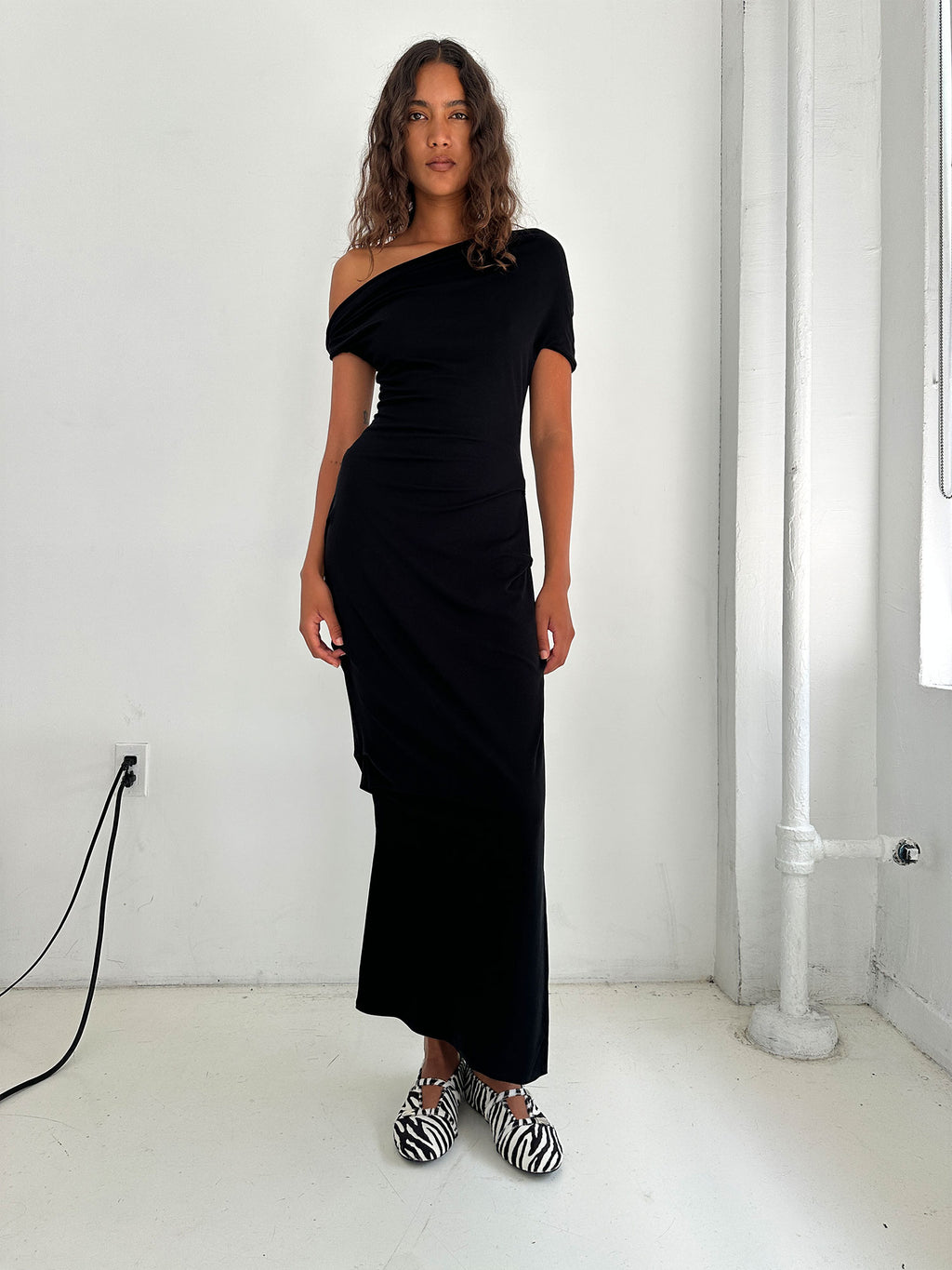 Model standing in front of a concrete wall wearing a Black Elemental Ida Dress