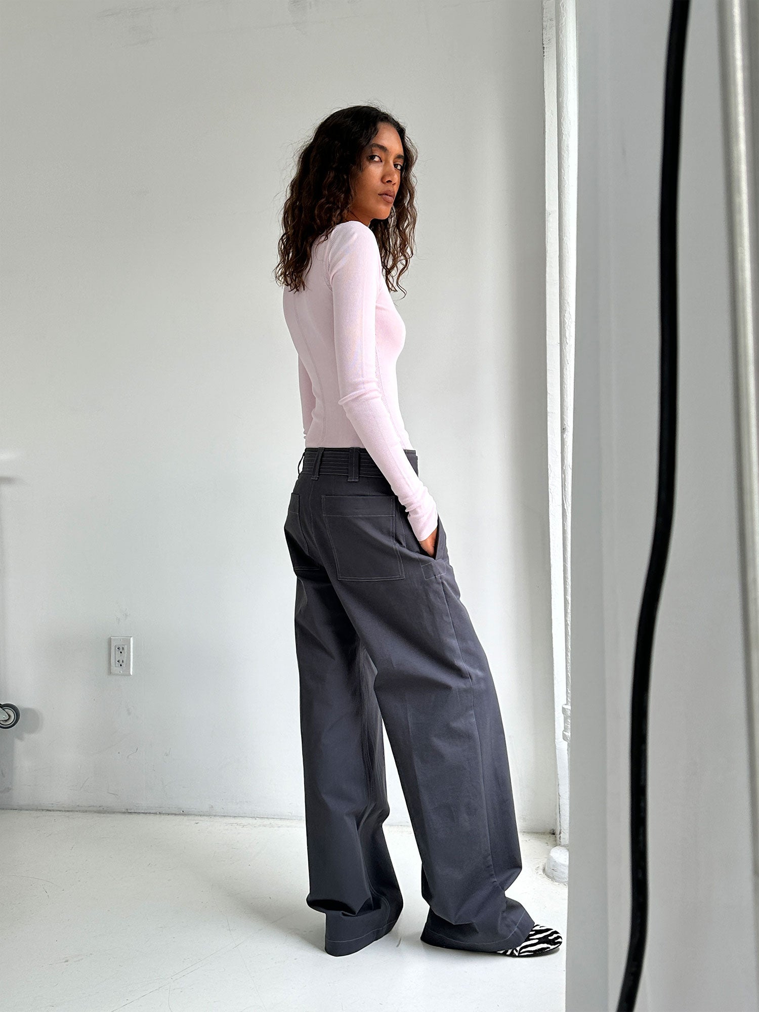 Model looking over her shoulder wearing a Pale Pink Elemental Second Skin Top and concrete trousers