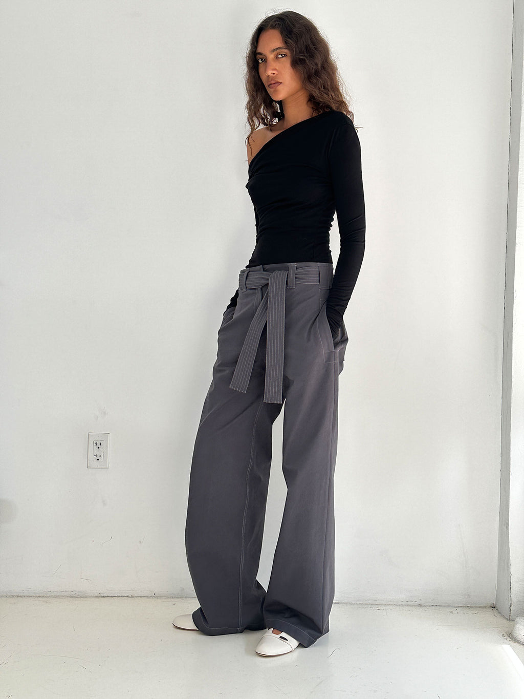 A model standing near a concrete wall wearing a Elemental Manahou Top in Black and grey trousers