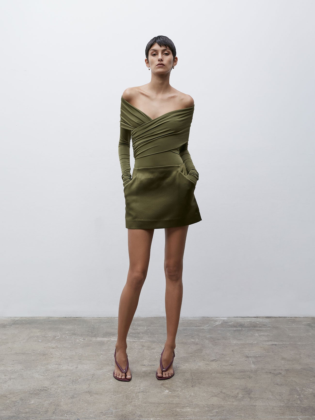 Front view of a model wearing a Olive 09 Cass Mini Skirt with her hands in the dress's pockets