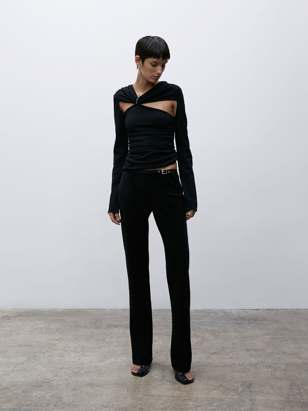 Front view of a model standing naturally but looking down and off to the side wearing Black 09 Sleek Belted Pants