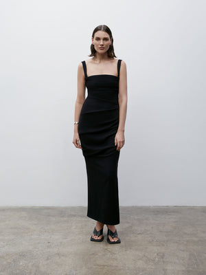 A model wearing a black dress and Black 08 Dune Wedge shoes