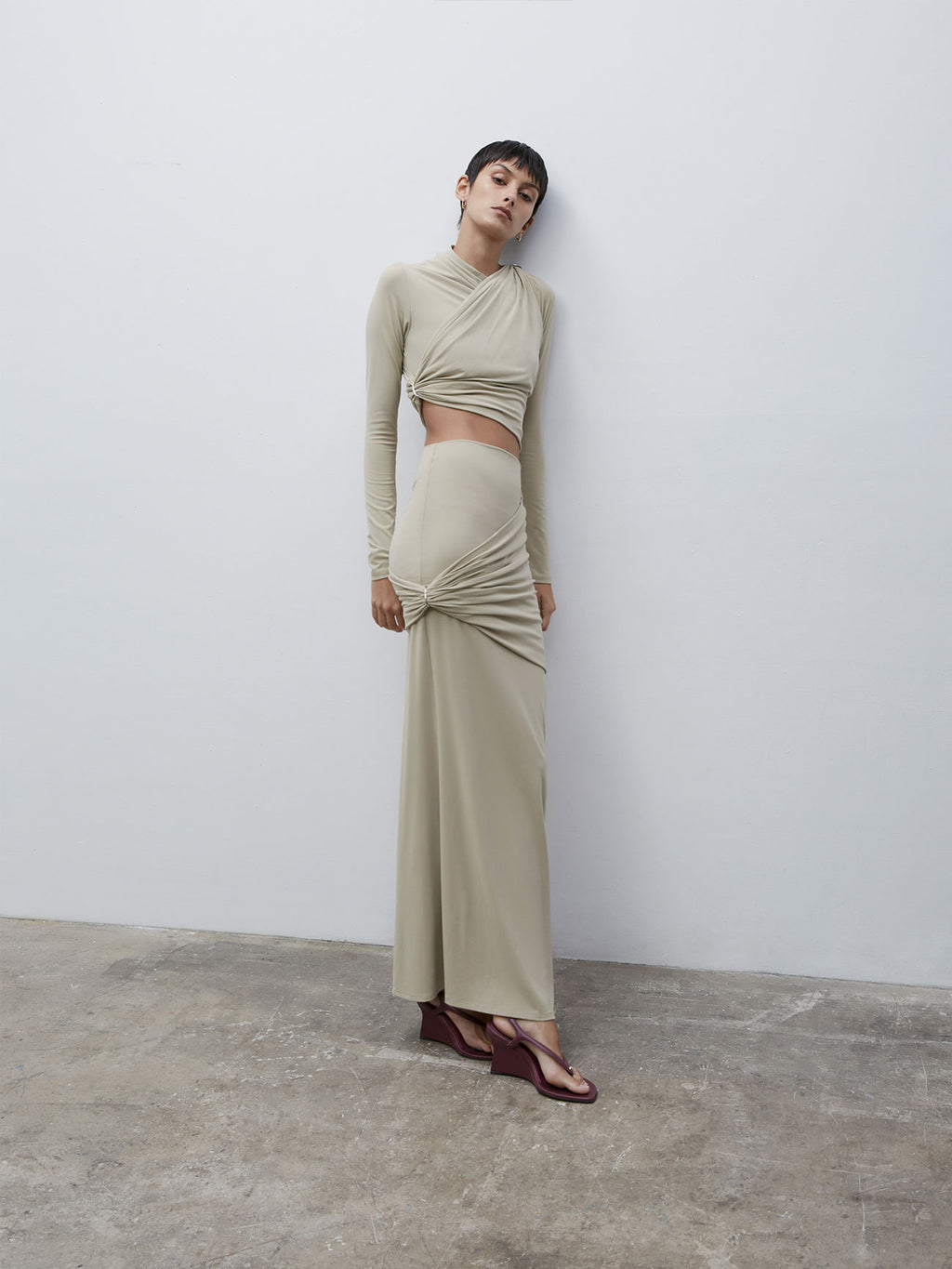 A female figure leaning back against a wall looking up at the camera wearing the Sand 09 Aria Top and matching skirt