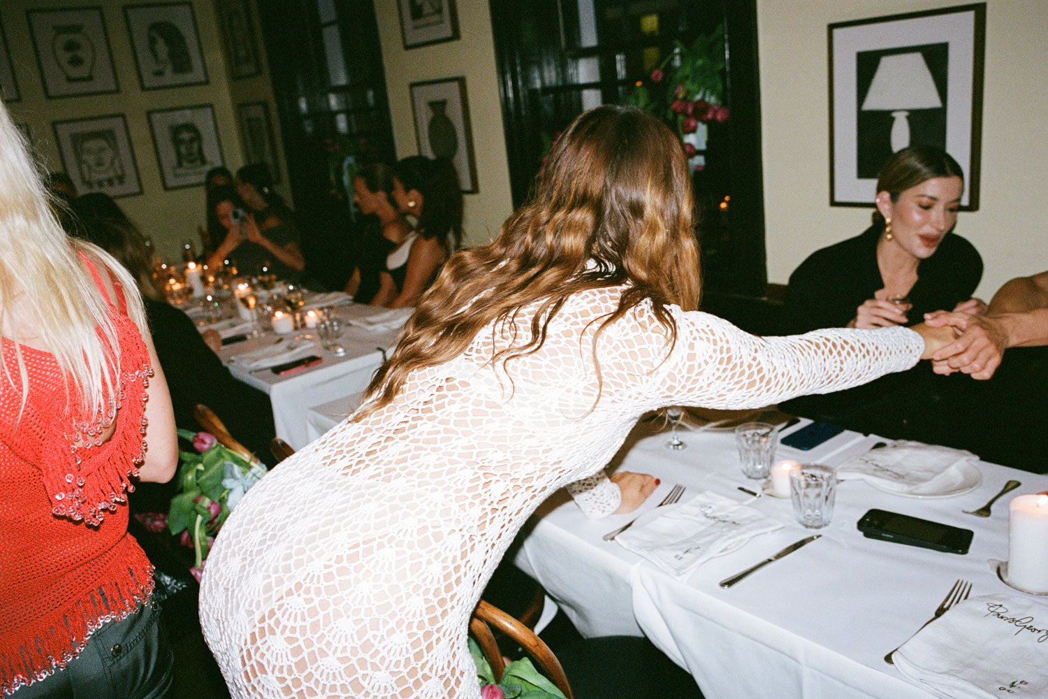 A female figure leaning over a restaurant table to shake hands wearing the White 09 Crochet Dress