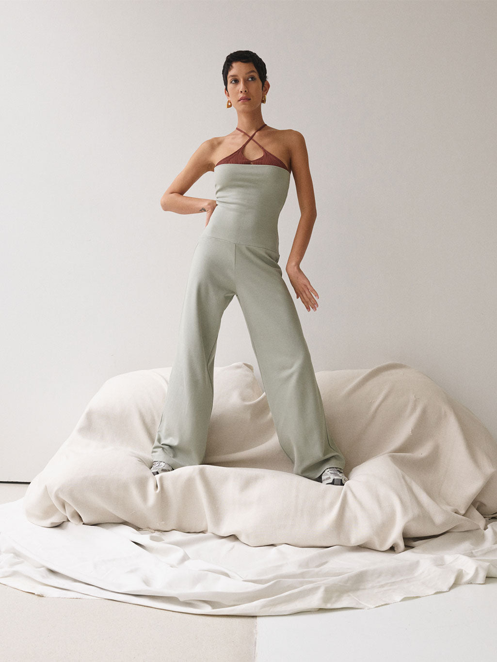 A woman standing wearing a sage-coloured jumpsuit.